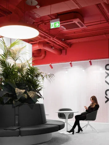 Moderne zithoek met planten, rode plafond en vrouw op smartphone in kantoorruimte
