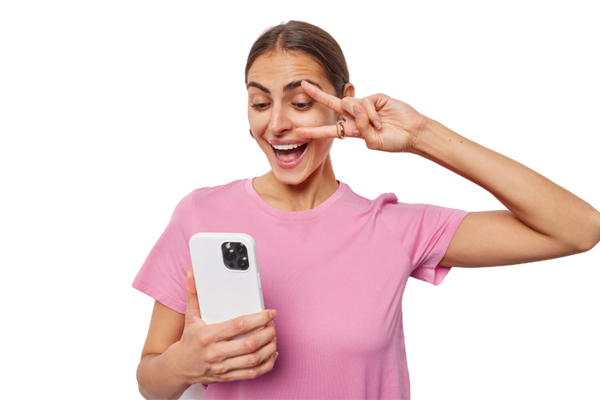 Vrouw in roze shirt glimlacht en maakt V-teken terwijl ze een iPhone vasthoudt